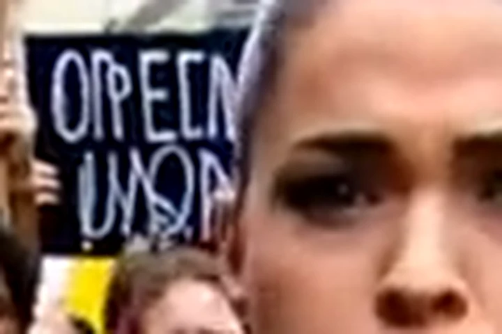 Close crop of a protest placard showing letterforms that read approximately OPPEEM UNOR and do not spell words