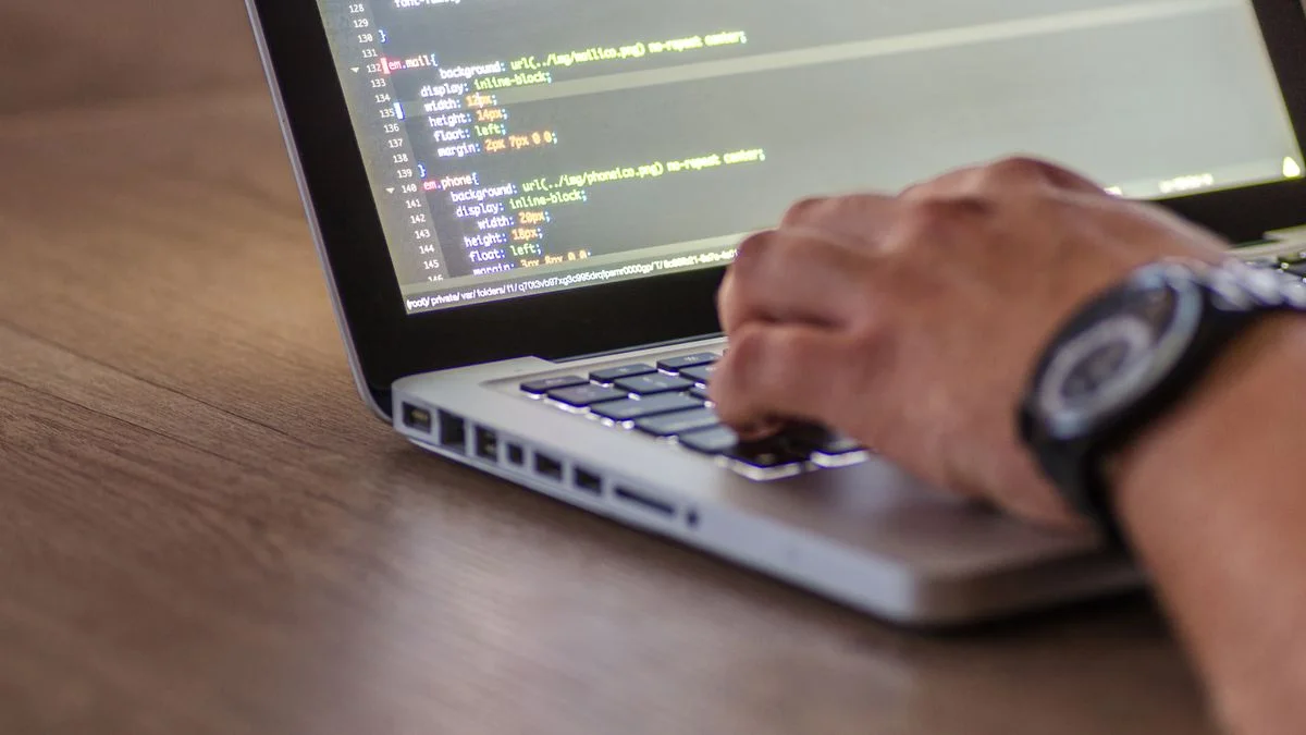 Close-up of a person's hands typing code on a laptop keyboard